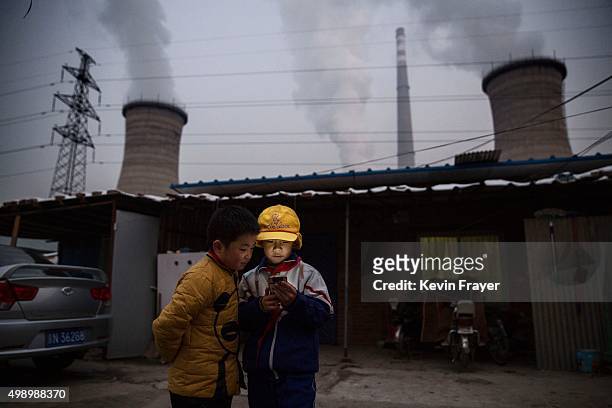 Chinese boys look at their smartphone in front of their house next to a coal fired power plant on November 27, 2015 on the outskirts of Beijing,...