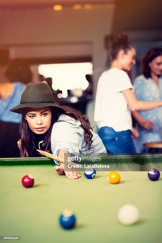 Mixed race young woman playing pool game in pub