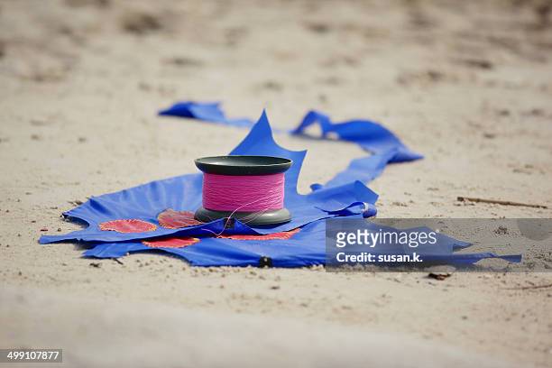 blue kite & string reel lying on the sandy beach. - indonesian kite stock pictures, royalty-free photos & images
