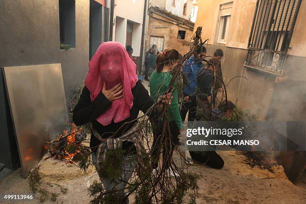 Woman covers her face with a piece of clothe as she carries branches to light a bonfire on November 29 in the northern Spanish village of Arnedillo...