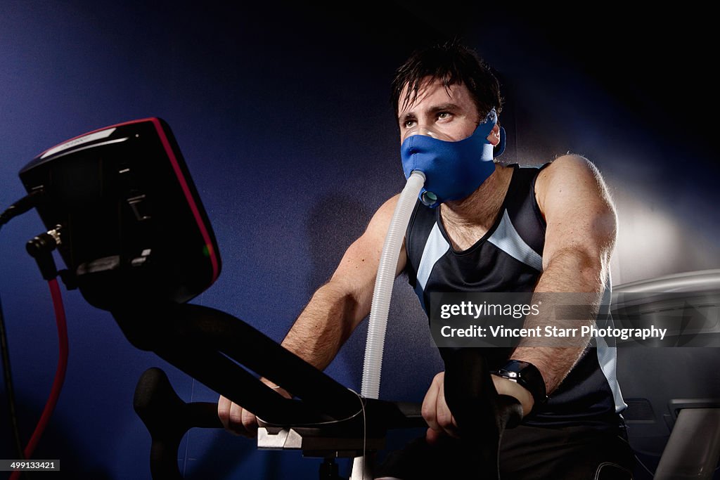 Mid adult man in face mask on gym exercise cycle in altitude centre