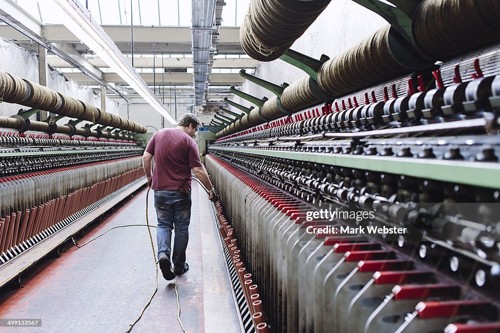 Male factory worker monitoring weaving machines in woollen mill