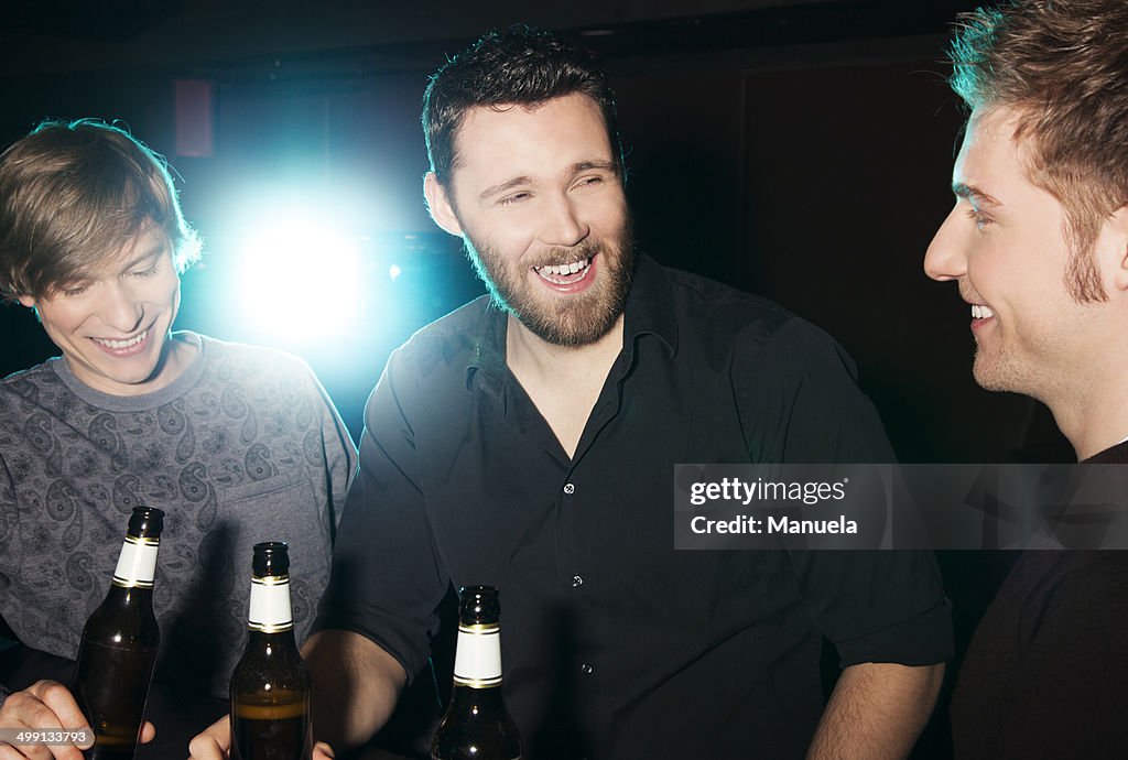 Three male friends drinking bottled beer in nightclub