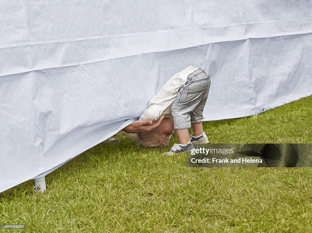 Young boy bending forward to reach fathers hand under tent