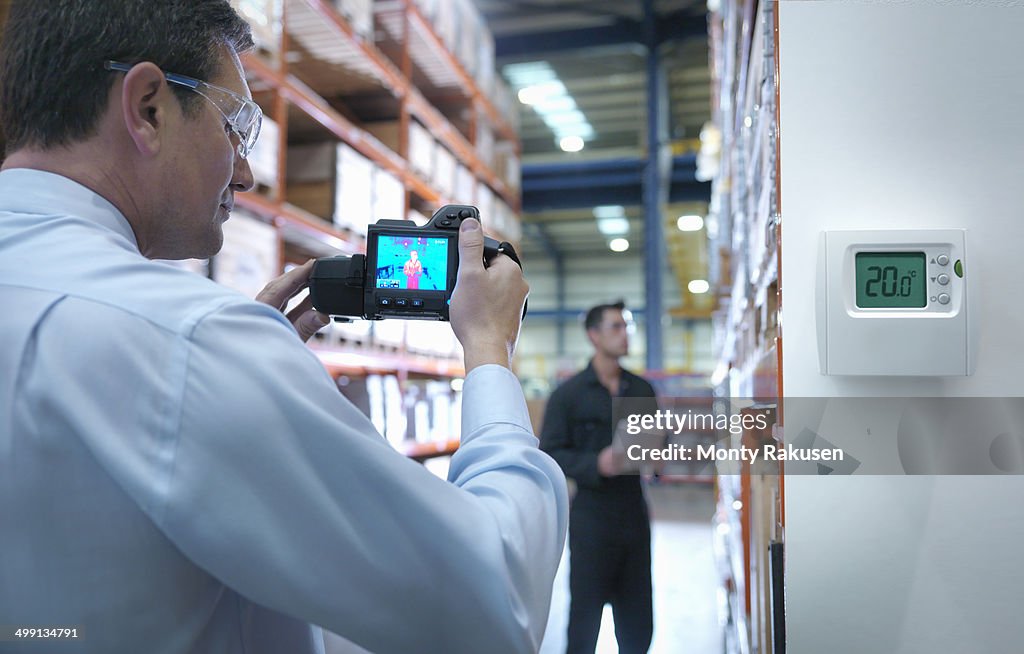 Office worker taking thermal image with camera in factory next to thermostat