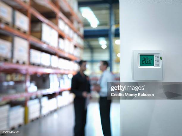 worker and office manager discuss energy use near thermostat in factory - temperature controlled storage stock pictures, royalty-free photos & images