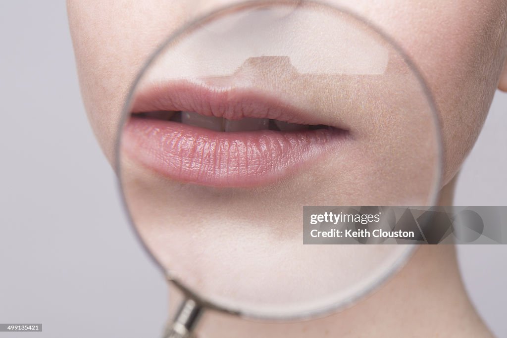 Portrait of young woman, magnifying glass on mouth