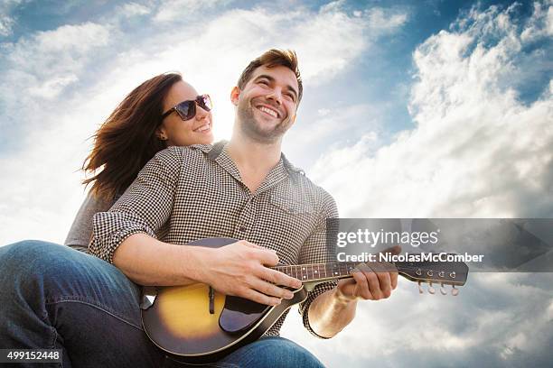 young couple smiling outoors while man plays country song - country and western music stock pictures, royalty-free photos & images