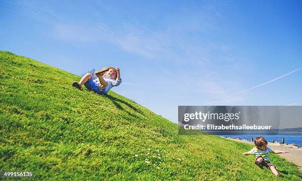 two boys (2-3, 3-4)  rolling down grassy hill - grass hill stock pictures, royalty-free photos & images