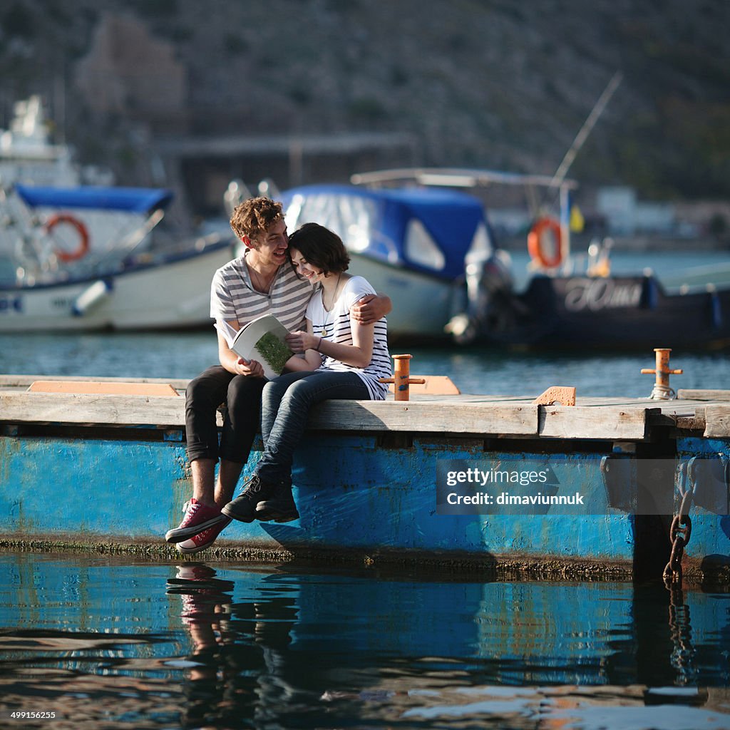 Teenage couple (14-15) sitting on jetty, embracing