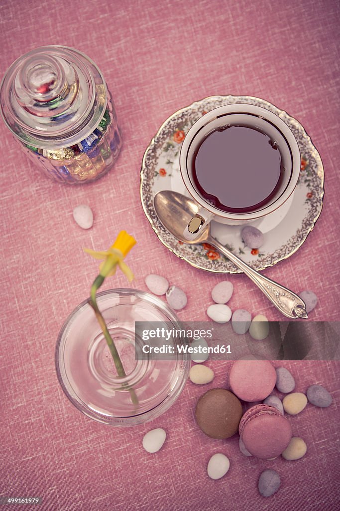 Laid table with cup of tea, daffodil (Narcissus pseudonarcissus), macarons and a glass of sweets, elevated view