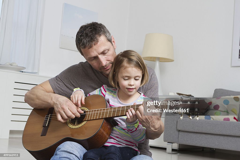 Father teaching daughter to play guitar