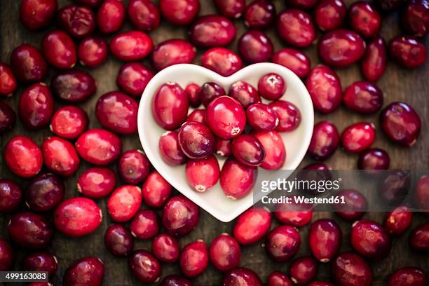 bowl of cranberries surrounded by cranberries on wooden table, elevated view - cranberry heart stock-fotos und bilder