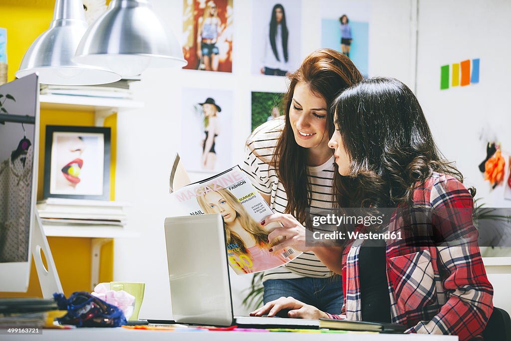 Two female fashion bloggers watching magazine at office