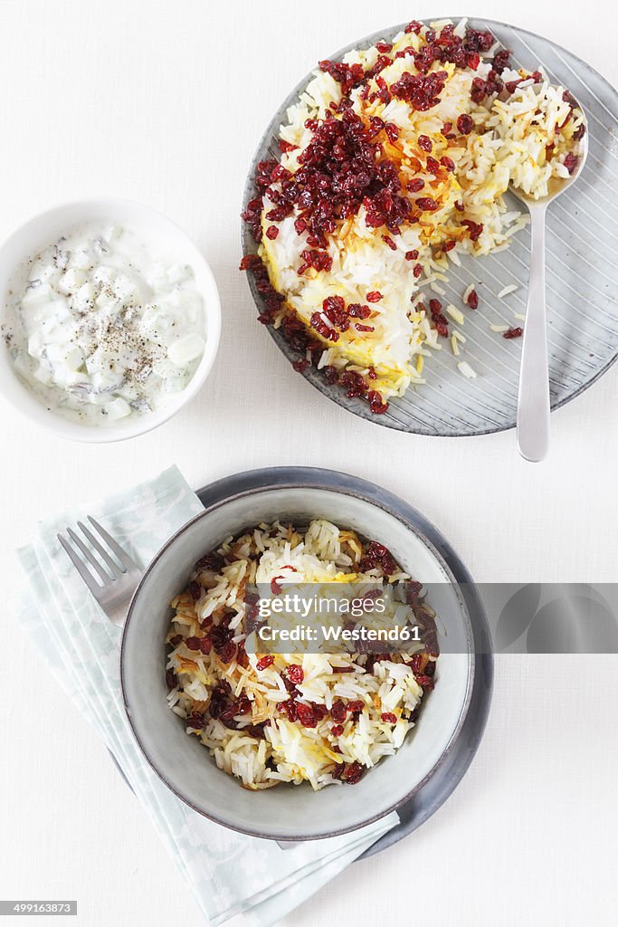 Persian saffron rice with barberries and bowl of mint yoghurt on white background
