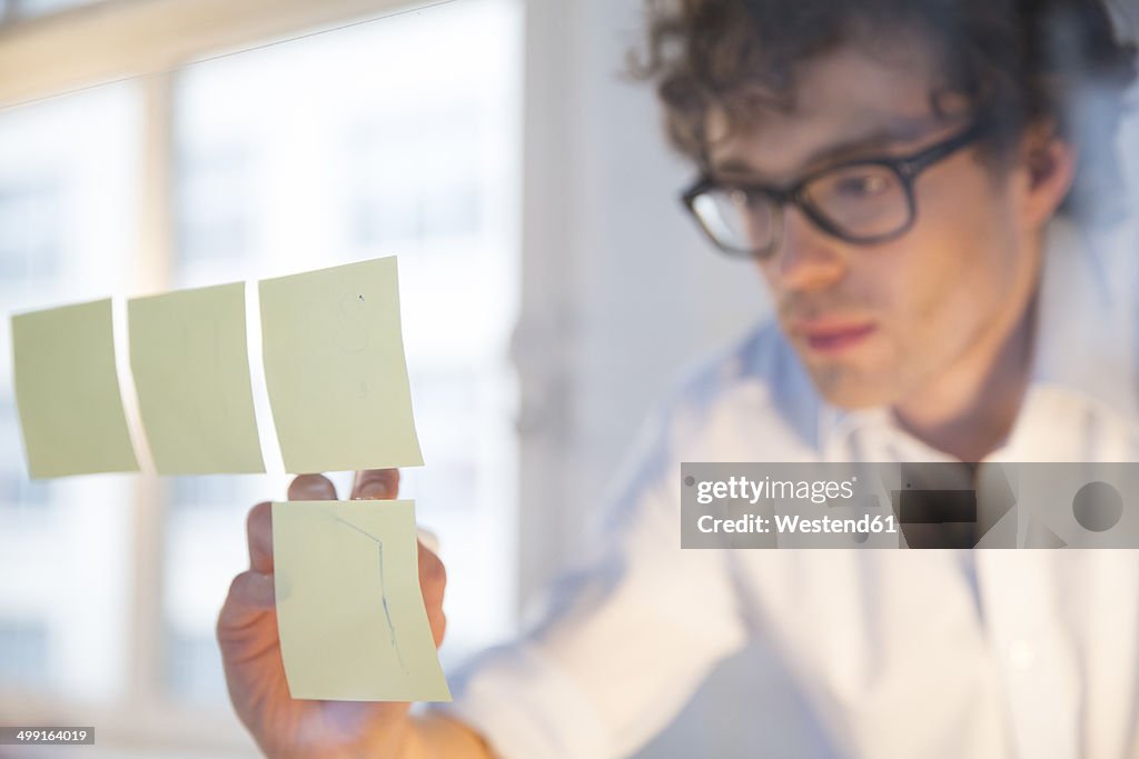 Portrait of young architect fastening memos on glass pane in office