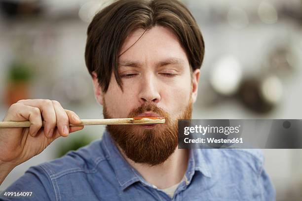 man cooking in kitchen tasting from wooden spoon - schmecken stock-fotos und bilder