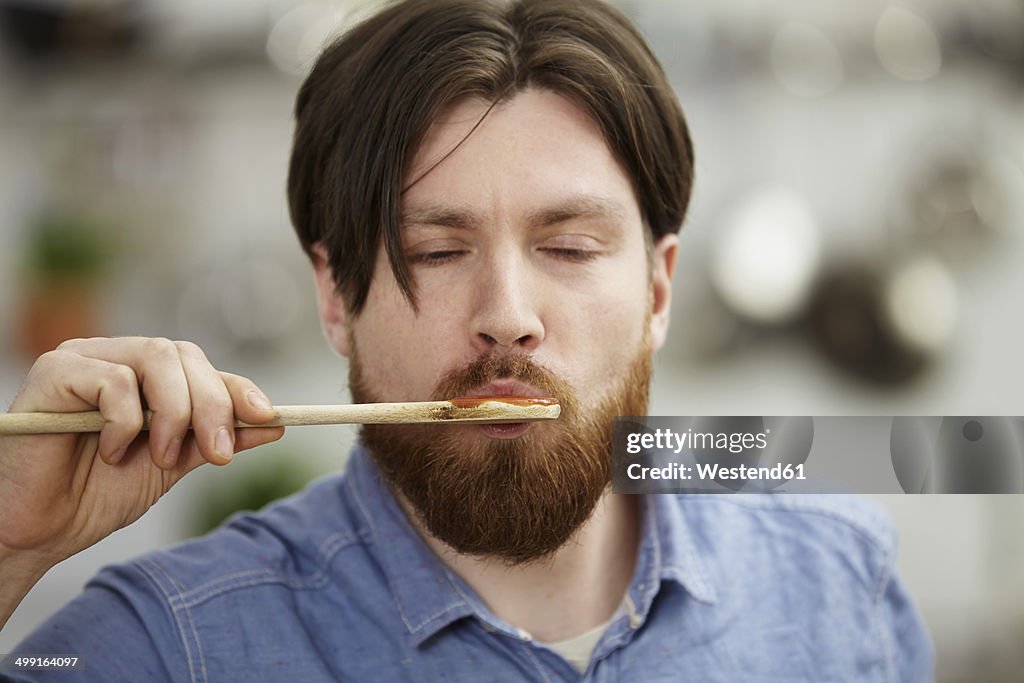 Man cooking in kitchen tasting from wooden spoon