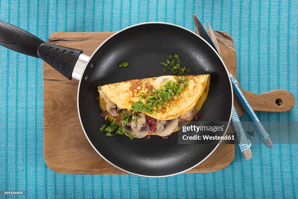 Omelette with champignon, onion and ham in frying pan