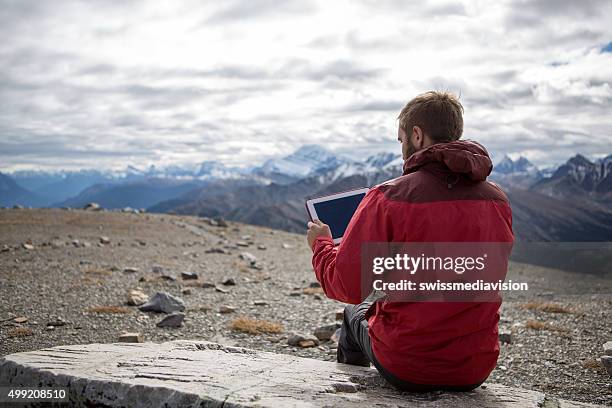 hiker on mountain top using a digital tablet - outdoor guy sitting on a rock stock pictures, royalty-free photos & images