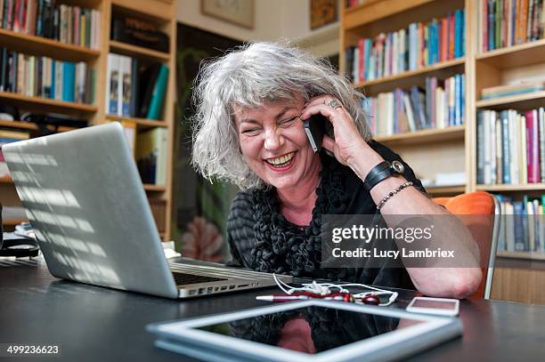 woman laughing on the phone at home office - mature women laughing stock pictures, royalty-free photos & images