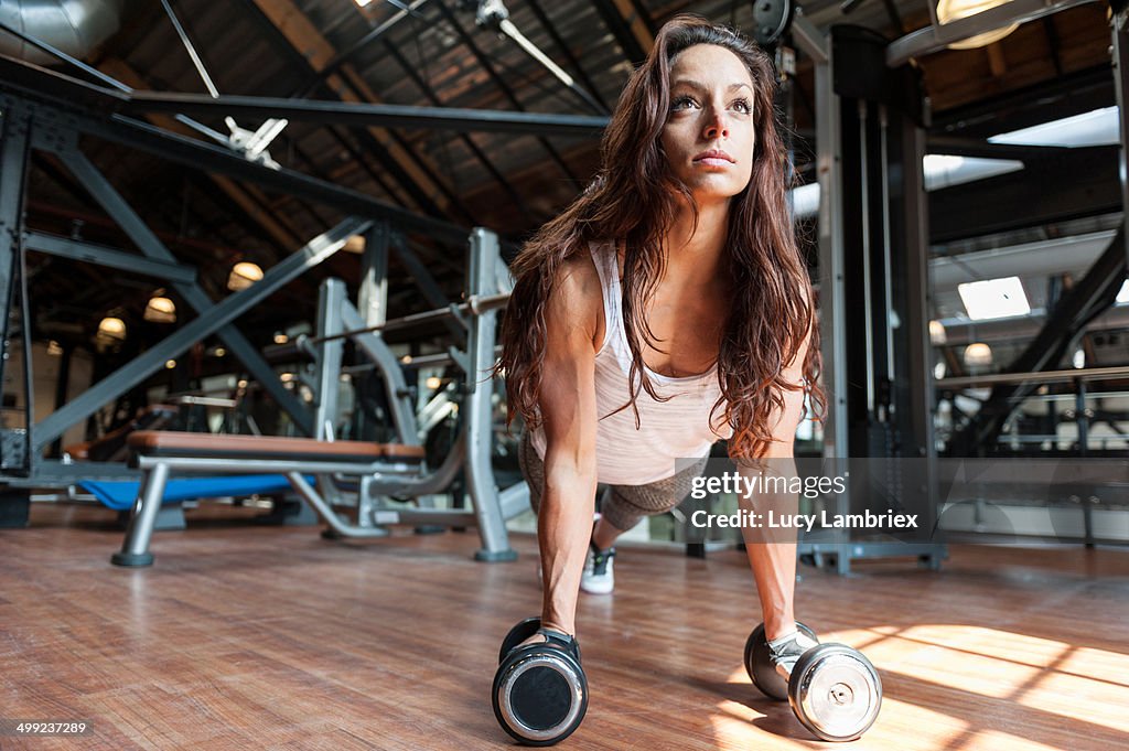 Young woman at gym doing pushups on dumbbells