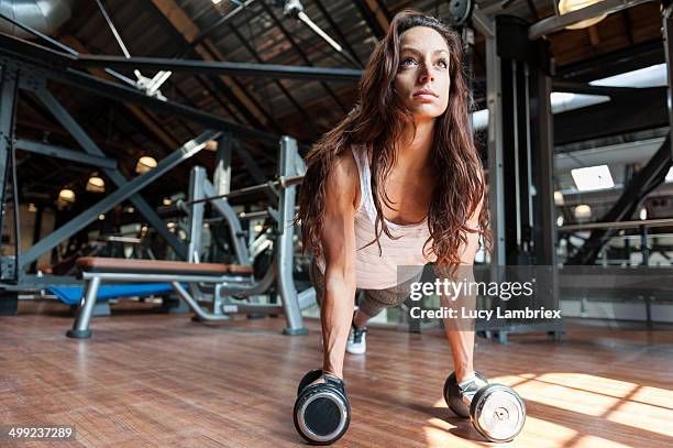young woman at gym doing pushups on dumbbells - trainingsraum stock-fotos und bilder