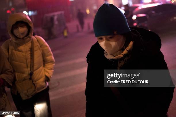 Pedestrians wear masks on a polluted evening in Beijing on November 30, 2015. Choking smog blanketed Beijing and much of northern China on November...