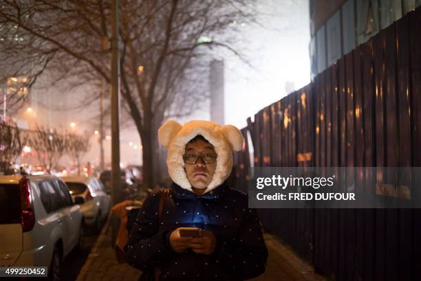 Man with a teddy bear hat walks along a street on a polluted evening in Beijing on November 30, 2015. Choking smog blanketed Beijing and much of...