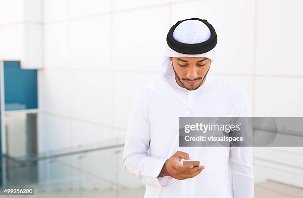 emirati businessman doing business on the go with smartphone - emirati man portrait stockfoto's en -beelden