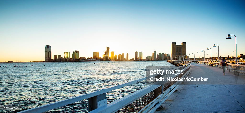 Weibliche jogger auf Manhattan pier mit Jersey City und den Sonnenuntergang