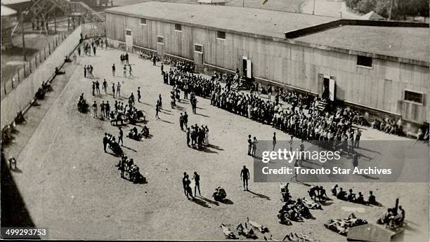 Left behind; A crowd of German prisoners lounge about the yard of a prison camp in the Sudbury area; from which an airman and a naval petty officer...