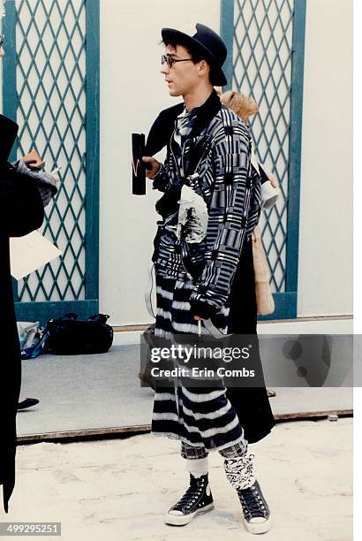 Below; the male skirt; worm with artfully mismatched hip sash; is accessorized with hat; scarf; socks; shoulder bag and basketball sneakers.