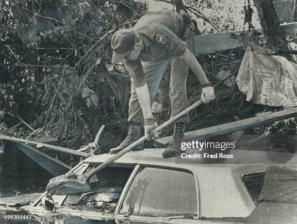 National Guardsman digs mud from a car in Rapid City; S. D. To see whether anyone was trapped inside when a cloudburst sent torrential flood roaring...