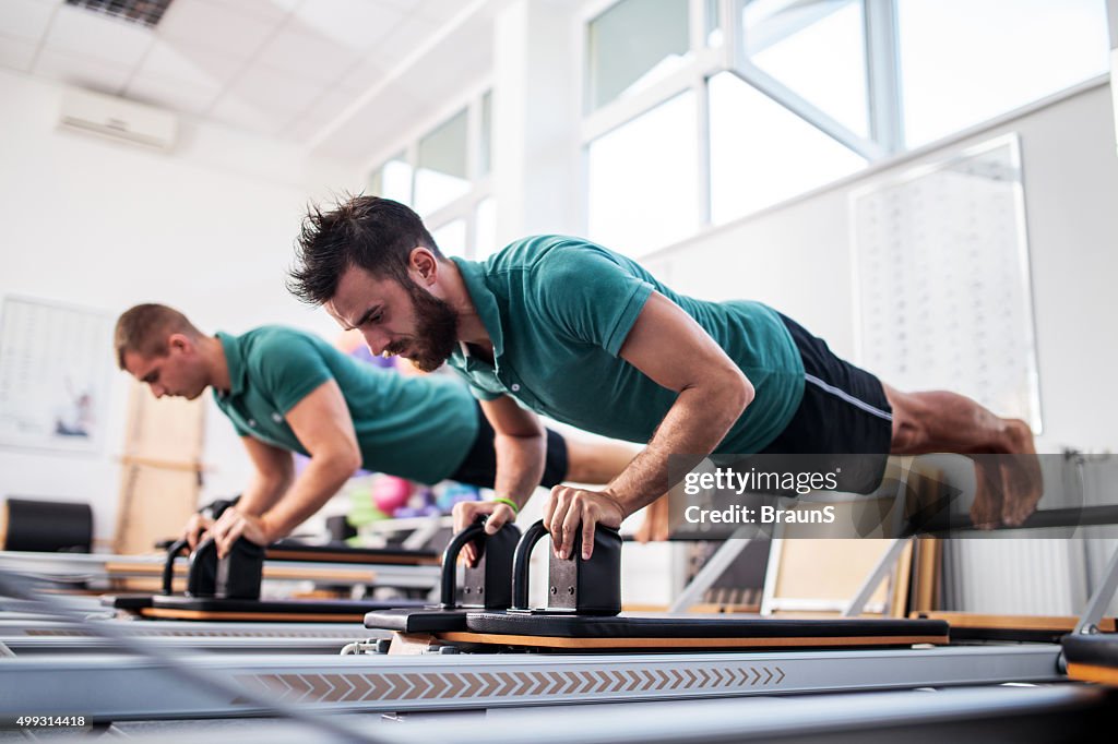 Dois homens jovens, tendo uma aula de Pilates em Clube de Saúde.