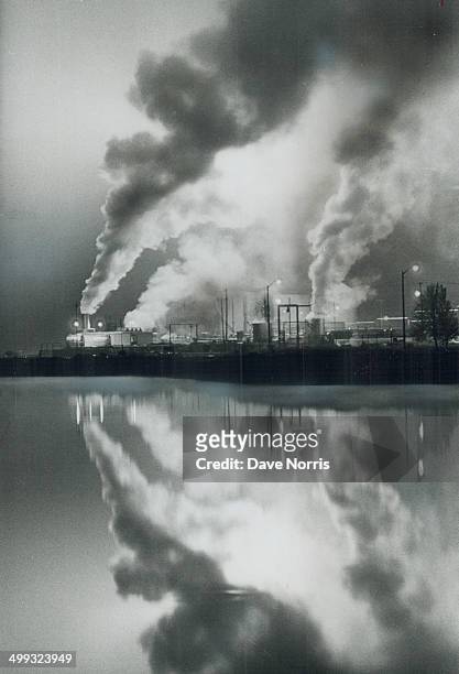 Mirroring a refinery; Spewing smoke into the air; the Texaco refinery at Port Credit is reflected in the glassy waters of an adjoining pond; created...
