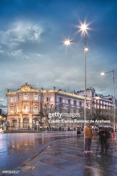 Lluvia en las calles de Madrid con gente con paraguas paseando por la ciudad al anochecer.
