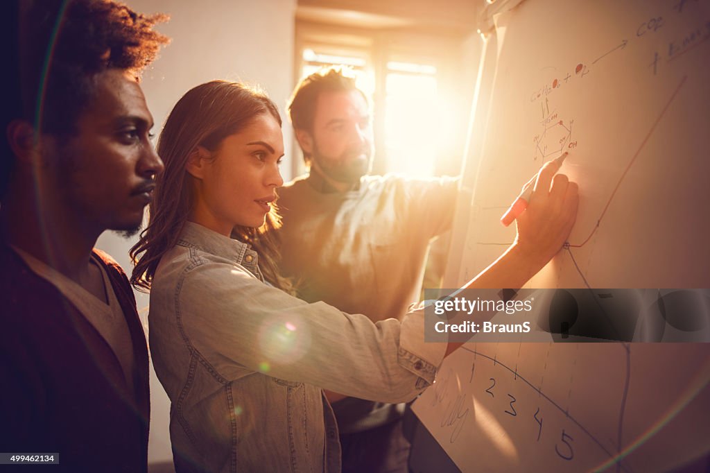 Businesswoman drawing a graph together with her two male colleagues.