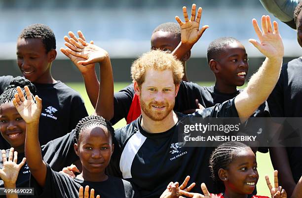 Britain's Prince Harry waves as he poses with children during a visit to the staff and management at the GrowthPoint Kings Park Stadium on December...