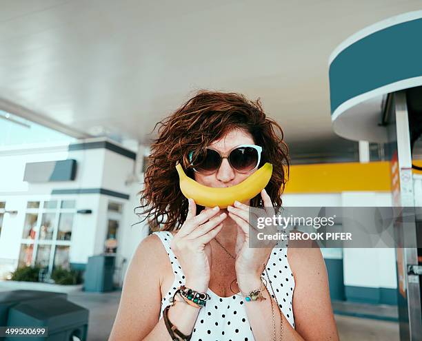 young woman holding banana up to face as a smile - banana woman photos et images de collection