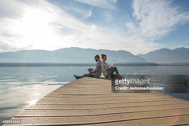 young couple relax on lake pier with book,digital tablet - roman landscapes stockfoto's en -beelden
