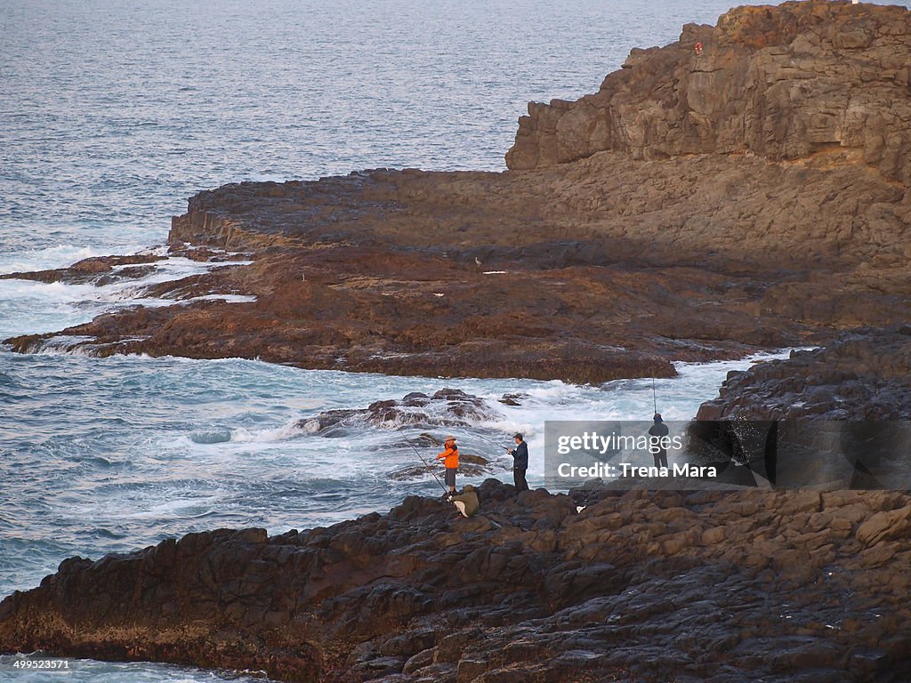 Men rock fishing at edge of ocean