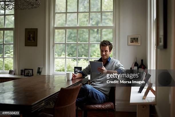 man surfing net on digital tablet in cottage - lezen stockfoto's en -beelden