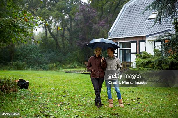 mother and daughter with umbrella outside cottage - mother protecting from rain stockfoto's en -beelden