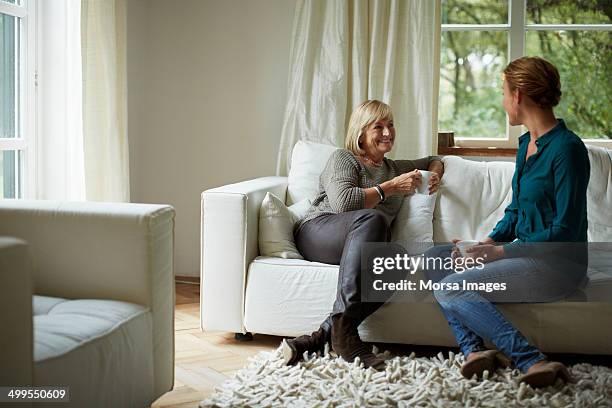 mother and daughter having coffee on sofa - woman home sit foto e immagini stock