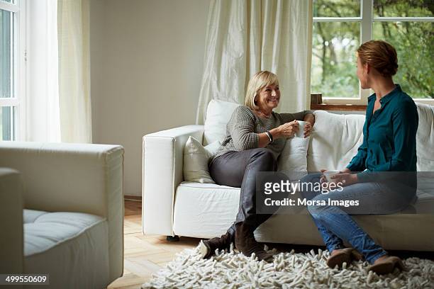 mother and daughter having coffee on sofa - fabulous full lengths stockfoto's en -beelden