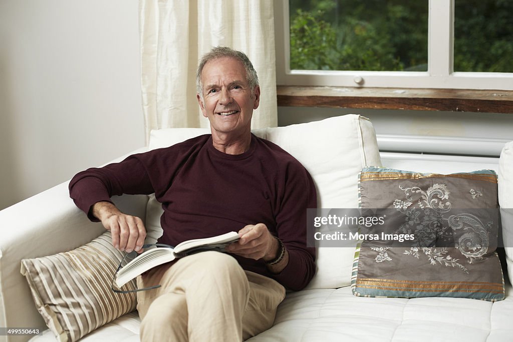 Confident senior man reading book on sofa