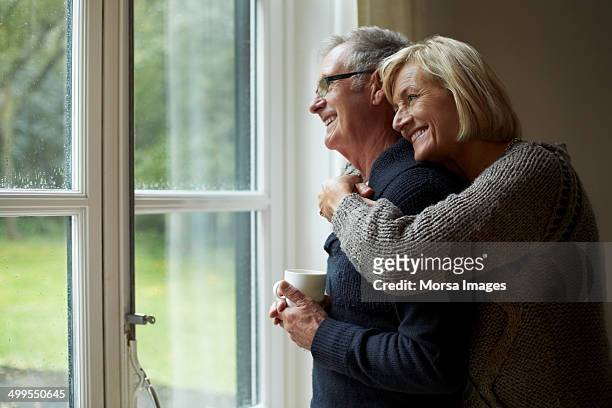 senior woman embracing man in front of door - coppia anziana foto e immagini stock