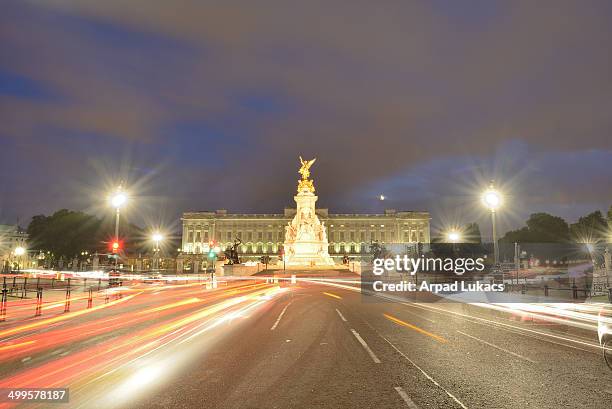 London's Buckingham Palace captured at night with Victoria Memorial in the center. A rising crescent Moon is slightly visible just above the building...