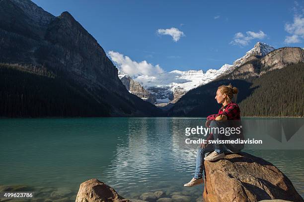 座る若い女性、ロック、湖のくつろぎ - lake louise ストックフォトと画像